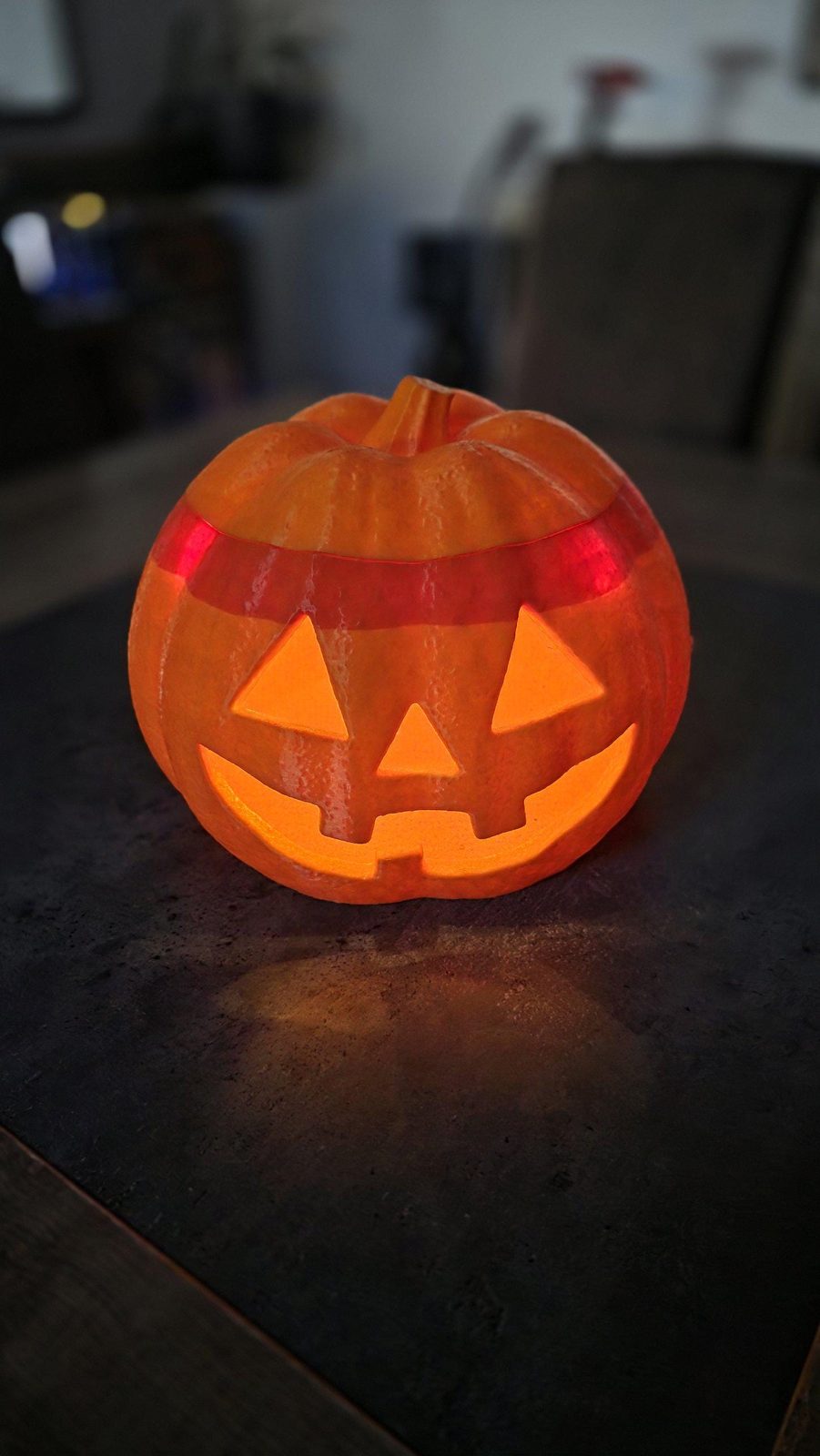 Citrouille lumineuse d'Halloween de face, posée sur une table sombre, visage découpé éclairé de l'intérieur